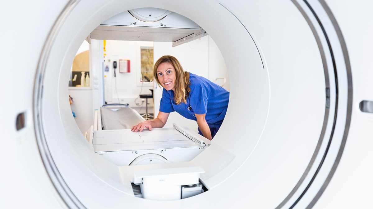 Leende kvinna i arbetskläder klicka fram vid en röntgenapparat.
