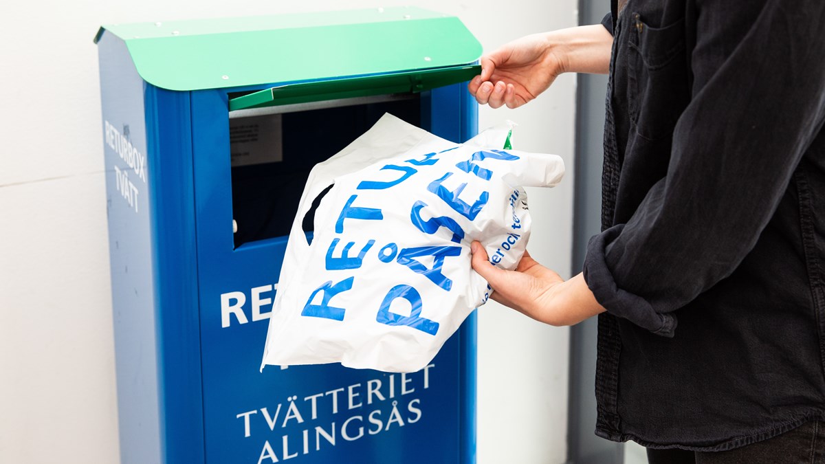 Person lägger en vit plastpåse med kläder i en returbox.
