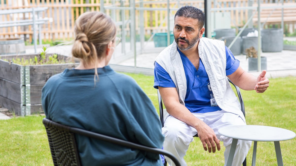 En psykiatrimedarbetare pratar med en patient. De sitter utomhus på varsina stolar.