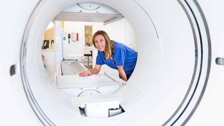 Kvinna i blå vårdkläder tittar fram i en röntgenapparat.
