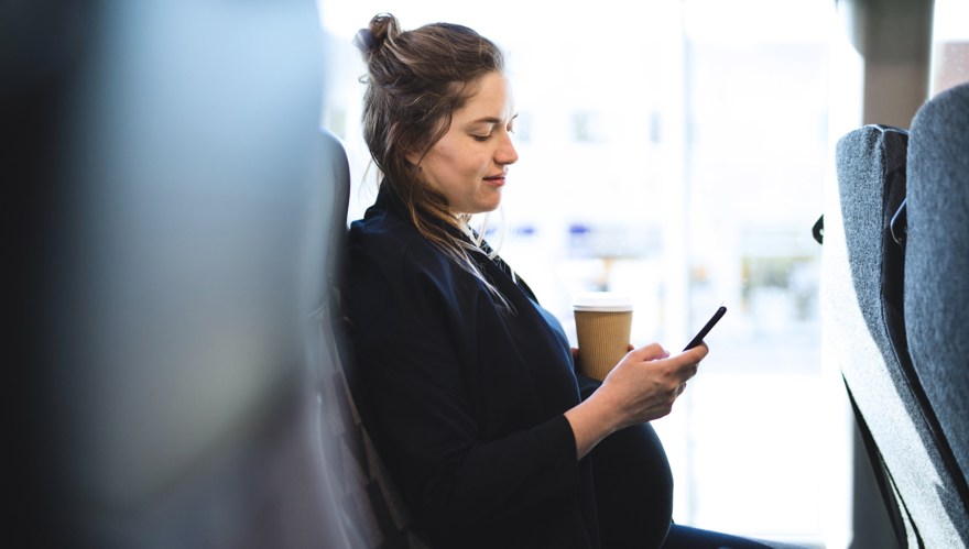 Gravid kvinna sitter på bussen och tittar på sin mobiltelefon.